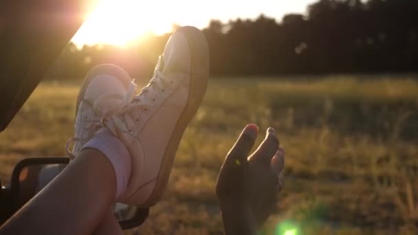 Jeune femme aime voyager dans une voiture, mettant ses jambes par une fenêtre ouverte. Jambes d'une fille dans une fenêtre de voiture, éblouissement du soleil, chevauchant une voiture sur une route de campagne . — Video