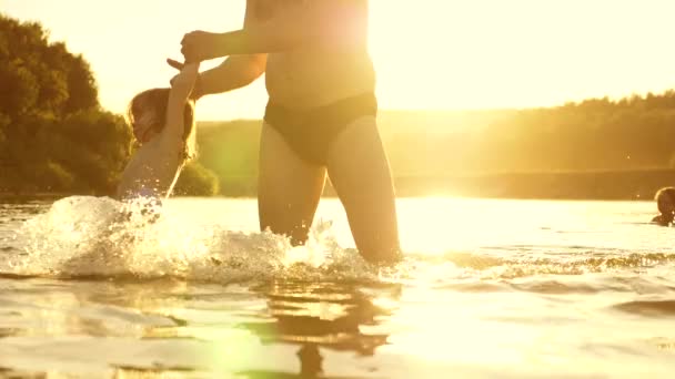 Buon papà e gioioso bambino sorridente, fare il bagno e giocare in acqua al tramonto dorato. padre e figlioletta stanno giocando in acqua sulla spiaggia al sole caldo . — Video Stock