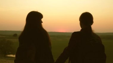 Kadın gezginler anne ve kızı sarılmak ve zafer zevk ve gün batımının tadını çıkarın. Yürüyüşçü Kız. Sırt çantaları olan takım çalışması yolcuları. Tatildeki turist ailesi. Seyahatler gün batımında manzaranın tadını çıkarır.