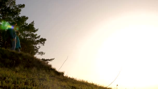 Mutter und Tochter reisen in den Urlaub. Frau mit erhobenen Händen auf einem Berg und Blick auf den Sonnenuntergang. Wandermädchen hebt die Hand, feiert den Sieg und genießt die schöne Landschaft und die Natur. — Stockvideo