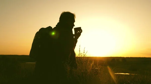 Viaggiatore beve tè caldo e guarda il tramonto. riposo dopo aver raggiunto l'obiettivo. turista solitario seduto in cima alla collina a bere caffè nel thermos. concetto di libertà e sogni. mondo senza frontiere — Foto Stock