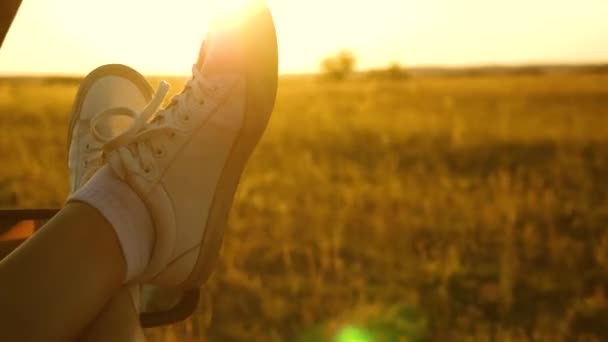 Woman travels by car. young woman likes to travel in a car, putting her legs out of an open window. Legs of a girl in a car window, glare of the sun, riding a car on a country road. — Stock Video