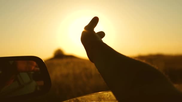 Motorista mão está brincando com o sol da janela do carro contra o pôr do sol bonito. Meninas mão acena o sol. Viajar de carro — Vídeo de Stock