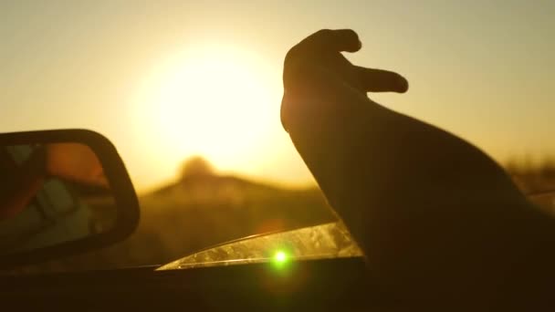 Meisjes hand golven de zon. Om met de auto te reizen. chauffeurs hand speelt met zon van auto venster tegen prachtige zonsondergang. — Stockvideo