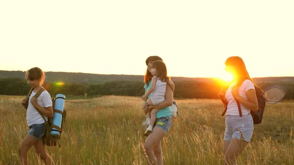 Glückliche Mädchen reisen im Sonnenuntergang über das Feld. Wanderin. Familie geht auf der Wiese spazieren. Mädchen sind mit Rucksäcken auf einer Landstraße unterwegs. glückliche Familie auf Urlaubsreisen. Sporttourismuskonzept — Stockfoto