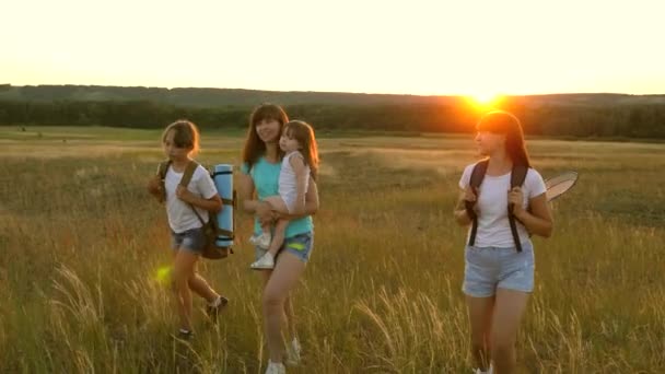 Moeder reist met haar dochters. moeder en kinderen zijn toeristen. meisjes reizen over veld in Sunset Light. Wandelaar meisje. familie wandelingen in de weide. meisjes reizen met rugzakken op een landweg. — Stockvideo