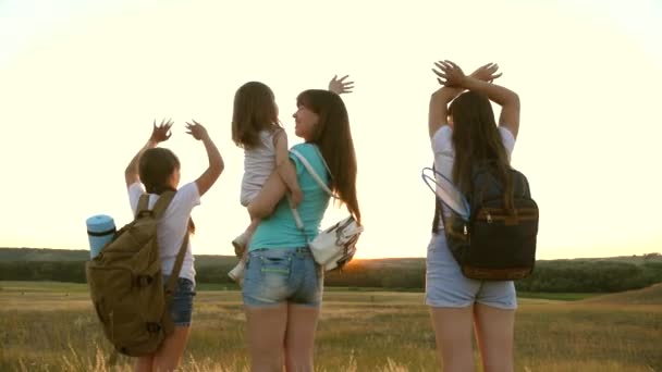 Mom travels with her daughters, admire the sunset and wave their hands. Mom and children are tourists. girls travel in the sunset light. Hiker Girl. girls travel with backpacks on a country road. — Stock Video