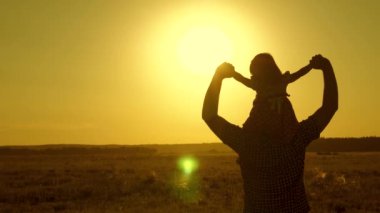 Küçük kız parkta omuzlarında babasıyla birlikte biniyor. Babam sevgili bebeğini gün batımında tarlada yürürken omuzlarında taşır. Ebeveyni olan çocuk akşam güneşin gün batımında yürür. Yavaş çekim.