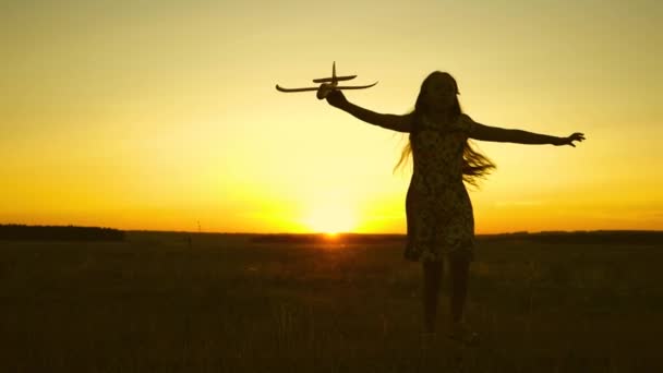 Ευτυχισμένο κορίτσι τρέχει με ένα αεροπλάνο παιχνίδι σε ένα πεδίο στο φως του ηλιοβασιλέματος. Τα παιδιά παίζουν παιχνιδάκια. έφηβος ονειρεύεται να πετάξει και να γίνει πιλότος. Το κορίτσι θέλει να γίνει πιλότος και αστροναύτης. Αργή κίνηση — Αρχείο Βίντεο