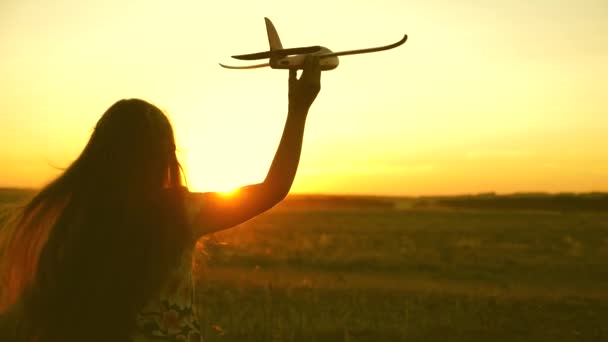 Ευτυχισμένο κορίτσι τρέχει με ένα αεροπλάνο παιχνίδι σε ένα πεδίο στο φως του ηλιοβασιλέματος. Τα παιδιά παίζουν παιχνιδάκια. έφηβος ονειρεύεται να πετάξει και να γίνει πιλότος. Το κορίτσι θέλει να γίνει πιλότος και αστροναύτης. Αργή κίνηση — Αρχείο Βίντεο