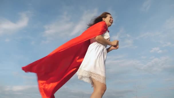 Divertida chica superhéroe correr y reír en capa roja, capa revoloteando en el viento. Joven alegre juega en super héroe. chica sueña con convertirse en un superhéroe. chica en una capa roja expresión de sueños . — Vídeo de stock