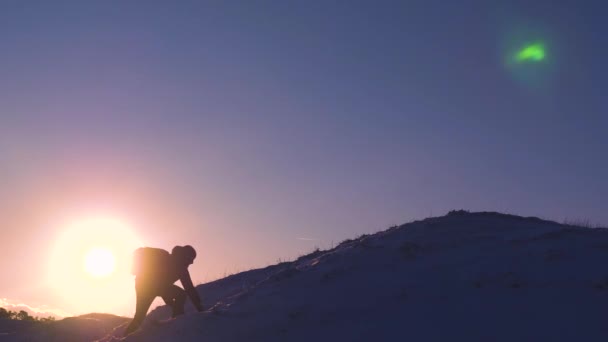 Touristes avec des sacs à dos s'aident mutuellement à grimper au sommet de la colline dans les rayons lumineux du soleil. Les grimpeurs sur une montagne enneigée se réjouissent de leur succès, lèvent la main et sautent heureux. concept de tourisme sportif . — Video