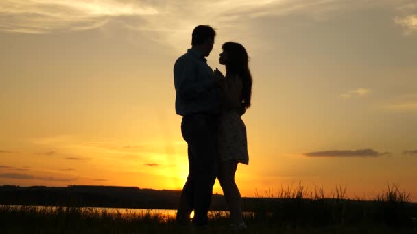 Pareja joven bailando al atardecer en la playa. Hombre y mujer cariñosos bailan en brillantes rayos de sol en el fondo del lago. Feliz chico y chica vals en la noche en el parque de verano . — Vídeos de Stock