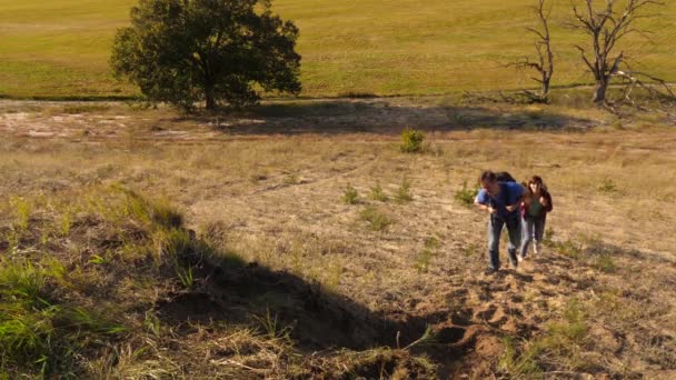 Pai estende a mão ajudando as crianças a subir a montanha. Família de turistas com crianças viajando ao pôr do sol. pai, crianças e mãe com mochilas viajam escalar montanha ao sol. trabalho de equipa turístico — Vídeo de Stock