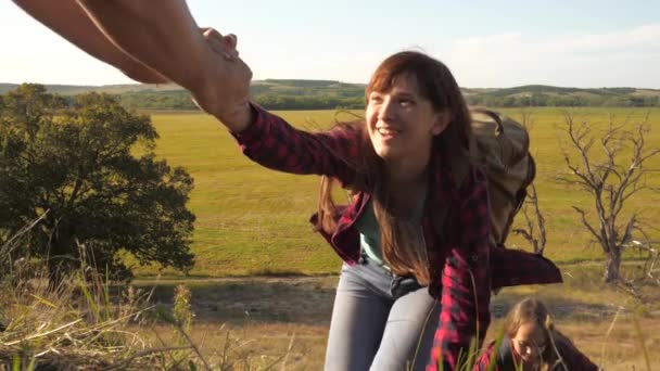 Pai estende a mão ajudando as crianças a subir a montanha. Família de turistas com crianças viajando ao pôr do sol. pai, crianças e mãe com mochilas viajam escalar montanha ao sol. trabalho de equipa turístico — Vídeo de Stock