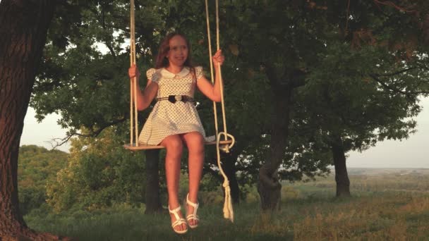 Bambino cavalca altalena corda su un ramo di quercia nella foresta. bella ragazza che oscilla su un'altalena sotto un albero al sole, giocando con i bambini. La ragazza ride, gioisce. Divertimento in famiglia nel parco, nella natura . — Video Stock