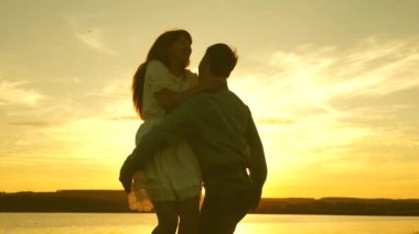 Mutlu adam ve kız yaz parkında akşam vals. Sevgi dolu erkek ve kadın gölün arka planda güneşin parlak ışınları dans. Genç çift sahilde gün batımında dans.