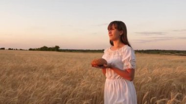 Genç bir kadının avuç üzerinde lezzetli ekmek. Kız onun avuç içi ekmek tutar ve olgun buğday alanı üzerinde gider. gün batımı ışınları bir buğday alanı üzerinde bir kızın ellerinde ekmek somun.