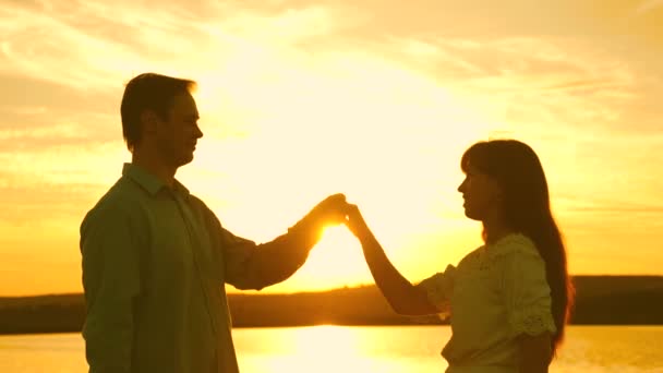 Mladí manželé tančí při západu slunce na pláži. Milující muž a žena tančí v jasných slunečních paprscích na pozadí jezera. Šťastný muž a dívka valčík večer v letním parku. — Stock video