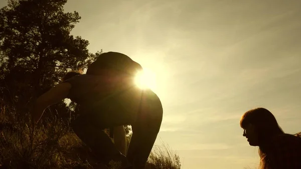 Padre tende la mano aiutando i bambini a scalare la montagna. Famiglia di turisti con bambini che viaggiano al tramonto. papà, bambini e mamma con gli zaini viaggiano scalando la montagna al sole. lavoro di squadra turistico — Foto Stock