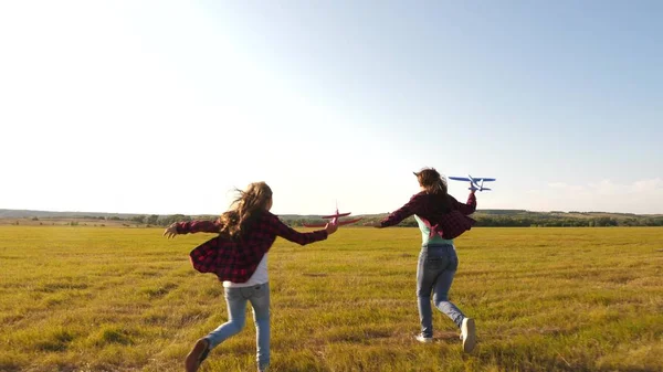 Marzenie o lataniu. Szczęśliwego dzieciństwa. Dwie dziewczyny bawią się zabawkowym samolotem o zachodzie słońca. Dzieci na tle słońca z samolotem w ręku. Sylwetka dzieci bawiących się w samolocie — Zdjęcie stockowe