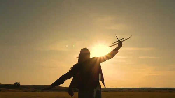 Glückliches Mädchen rennt mit einem Spielzeugflugzeug auf einem Feld im Sonnenuntergang. Kinder spielen Spielzeugflugzeug. Teenager träumt davon zu fliegen und Pilot zu werden. Das Mädchen will Pilotin und Astronautin werden. Zeitlupe — Stockfoto