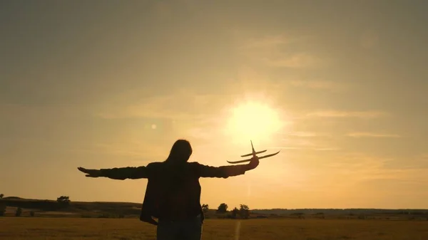 Chica feliz corre con un avión de juguete en un campo en la luz del atardecer. niños juegan juguete avión. adolescente sueña con volar y convertirse en piloto. la chica quiere convertirse en piloto y astronauta. Movimiento lento — Foto de Stock