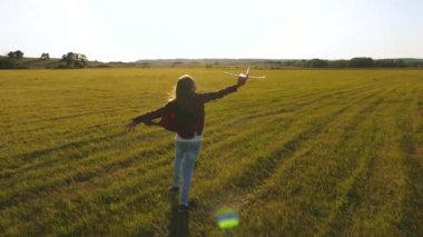 kız pilot ve astronot olmak istiyor. Yavaş çekim. uçan ve pilot olma genç hayalleri. Mutlu kız gün batımı ışığında bir alanda bir oyuncak uçak ile çalışır. çocuklar oyuncak uçak oynamak.