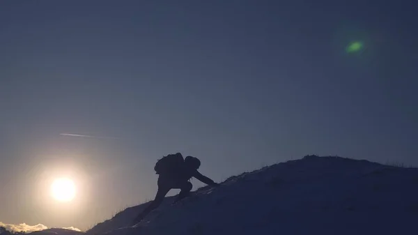 Dağcı kışın dağlara yolculuk. Gezgin dağ zirvesine tırmanıyor. turist yüksek karlı bir dağ üzerinde duruyor, ellerini dalgalar ve gün batımında zafer sevinir. Alpenist yürüyüş seyahat. — Stok fotoğraf