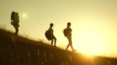 Gün batımında seyahat eden çocuklu turist ailesi. sırt çantaları olan çocuklar ve anne güneş ışınlarıdağlardan aşağı seyahat. Anne ve kızları kampa gidiyor. turistlerin ortak çalışma. Yavaş çekim