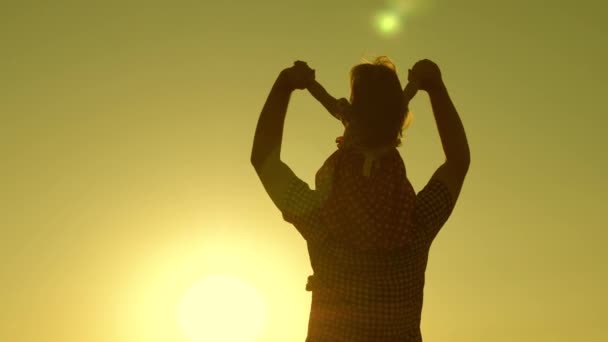 Dad carries beloved baby on his shoulders walking around field at sunset. little daughter riding with dad on his shoulders in park. A child with parent walks in evening at sunset of sun. Slow motion. — Stock Video