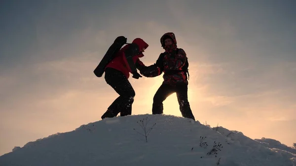 Teamarbeit und Sieg. Touristen reichen einem Freund die Hand, der auf den Gipfel des Hügels steigt. Bergsteiger im Winter auf verschneiten Bergen arbeiten in Kamanda, um einen Hügel zu erklimmen. Sporttourismuskonzept. — Stockfoto