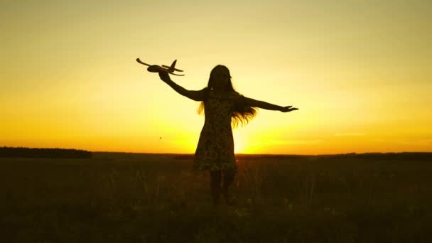 Menina feliz corre com um avião de brinquedo em um campo sob a luz do pôr do sol. As crianças brincam de avião de brinquedo. sonho adolescente de voar e se tornar piloto. a menina quer se tornar piloto e astronauta. Movimento lento — Vídeo de Stock