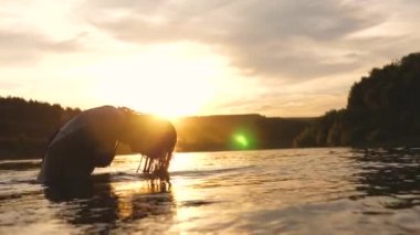 neşeli kız ferahlatıcı bir nehir suyu ile tropikal adanın yakınında ferahlatıcı bir yaz akşamı onu uzun saçları sıçraması. Kız geri saç çevirir. gün batımı ışınları su güzel sprey. su sıçrama