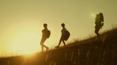 Gün batımında seyahat eden çocuklu turist ailesi. sırt çantaları olan çocuklar ve anne güneş ışınlarıdağlardan aşağı seyahat. Anne ve kızları kampa gidiyor. turistlerin ortak çalışma. Yavaş çekim