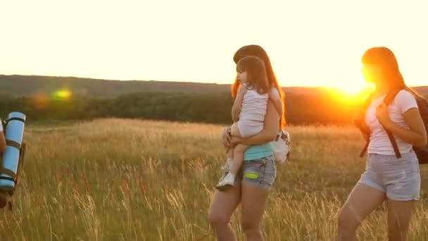 Happy girls travel across field in the sunset light. Hiker Girl. family walks in meadow. girls travel with backpacks on a country road. Happy family on vacation travels. sport tourism concept — Stock Video