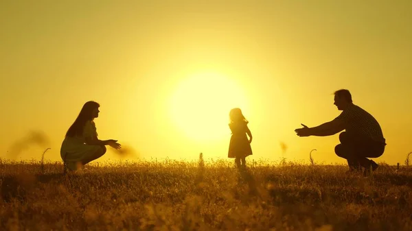 Батьки грають зі своєю маленькою донькою. Мати і тато грають зі своєю донькою на сонці. щаслива дитина йде від тата до мами. молода сім'я в полі з дитиною 1 рік. концепція сімейного щастя . — стокове фото