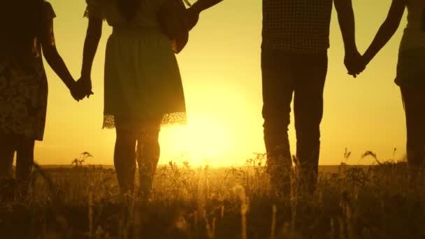 Familia feliz camina en el campo en la luz del atardecer. papá mamá e hijas están caminando en el parque a la luz del sol. niños y padres viajan de vacaciones. feliz padre lleva un niño — Vídeo de stock