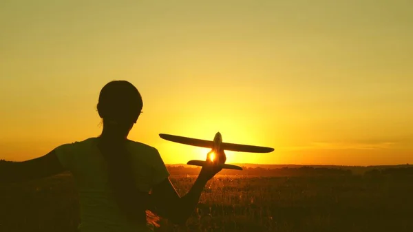 Barn leker leksaksflygplan. Happy Girl körs med en leksak flygplan på ett fält i solnedgången ljus. tonåring drömmer om att flyga och bli pilot. flickan vill bli pilot och astronaut. — Stockfoto
