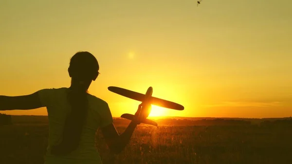 Niños juegan juguete avión. Chica feliz corre con un avión de juguete en un campo en la luz del atardecer. adolescente sueña con volar y convertirse en piloto. la chica quiere convertirse en piloto y astronauta . — Foto de Stock