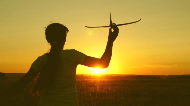 çocuklar oyuncak uçak oynarlar. Mutlu kız gün batımı ışığında bir alanda bir oyuncak uçak ile çalışır. uçan ve pilot olma genç hayalleri. kız bir pilot ve astronot olmak istiyor.