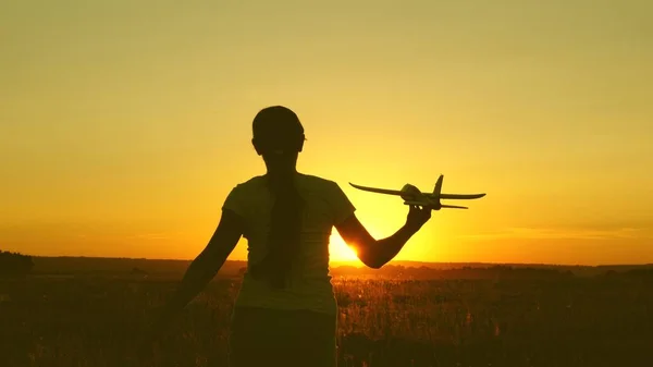 children play toy airplane. Happy girl runs with a toy airplane on a field in the sunset light. teenager dreams of flying and becoming pilot. the girl wants to become a pilot and astronaut.
