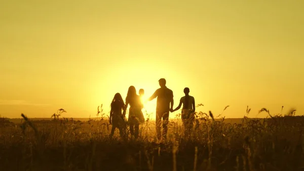 Happy family walks in field in sunset light. dad mom and daughters are walking in park in the light of sun. children and parents travel on vacation. happy father carries a child — Stock Photo, Image