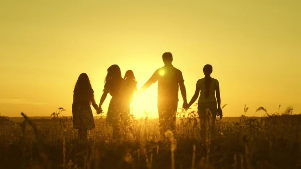 mutlu aile gün batımı ışığında alanda yürüyor. Baba anne ve kızları güneşin ışığında parkta yürüyorlar. çocuklar ve ebeveynler tatilde seyahat. mutlu baba bir çocuk taşır