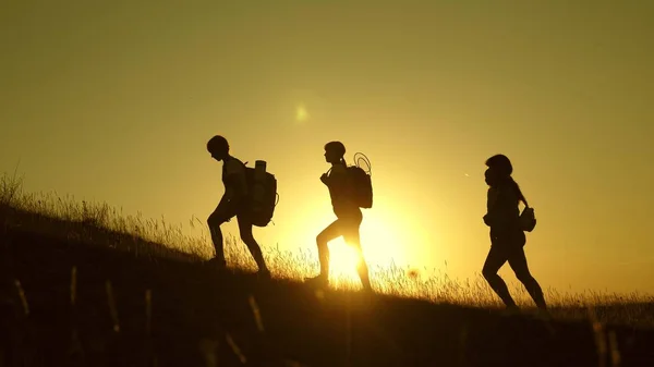 Bambini e mamma con zaini viaggiano scalano la montagna al sole. mamma e figlie vanno in campeggio. Famiglia di turisti con bambini che viaggiano al tramonto. lavoro congiunto dei turisti. movimento verso la vittoria . — Foto Stock