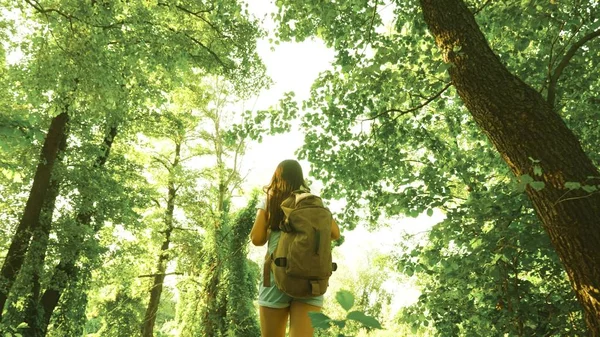 Vandrare flicka i sommarpark. tonåring flicka äventyr på semester. Girl Traveler går genom skogen med en ryggsäck och är glad att sprida sina armar ut till sidor. Vandrare kvinna promenader i skogen. — Stockfoto