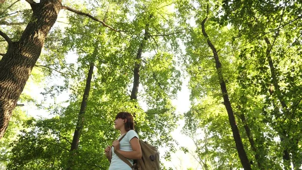 Hiker woman walks in the forest. Girl traveler is walking through the woods with a backpack. happy hiker girl in summer park. teenager girl adventures on vacation.