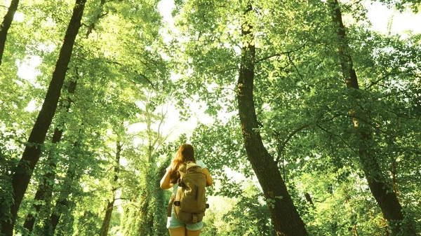 Wandelaar meisje in zomerpark. tiener meisje avonturen op vakantie. Meisje reiziger loopt door bossen met een rugzak en is gelukkig het verspreiden van haar armen naar de zijkanten. Wandelaar vrouw wandelingen in bos. — Stockfoto
