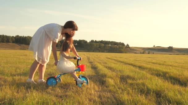 Mamma lär dotter att rida en cykel. dotter och mor spelar på ängen. Mamma leker med sin lilla dotter. ett litet barn lär sig att cykla. begreppet lycklig barndom. — Stockvideo