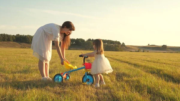 Mutter bringt Tochter Fahrradfahren bei. Mutter spielt mit ihrer kleinen Tochter. ein kleines Kind lernt Fahrrad fahren. Konzept einer glücklichen Kindheit. — Stockfoto
